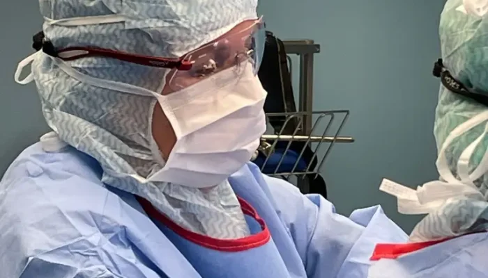 Foto van een close-up van Petra in operatie kleding, inclusief mondkapje, bril, muts en schort.