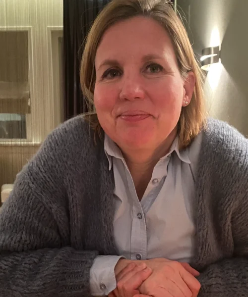 Close-Up van Petra, kijkend in de camera met een grijs vest en lichtblauwe blouse.